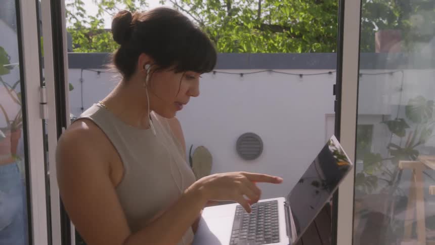 Woman talking on a call on her laptop while walking through the living room
