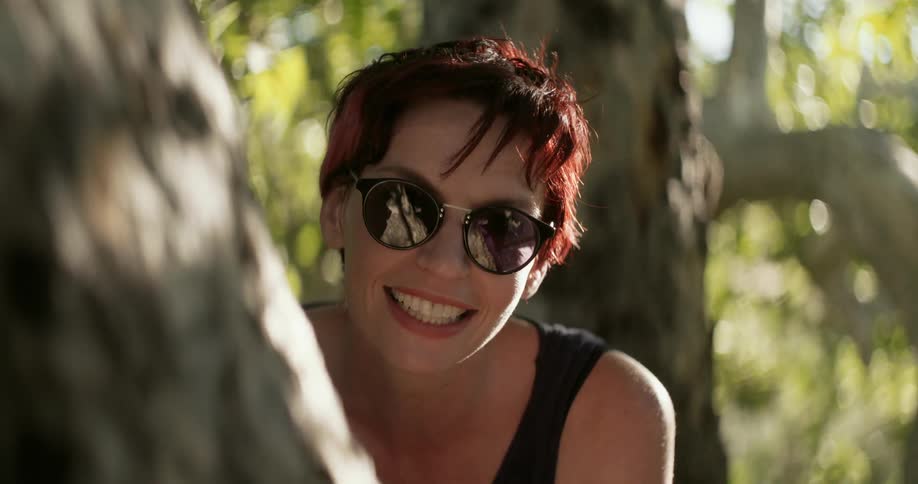 A woman looks around a tree and smiles