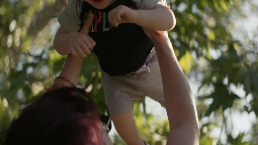 A woman is tossing and catching a toddler outside in daylight