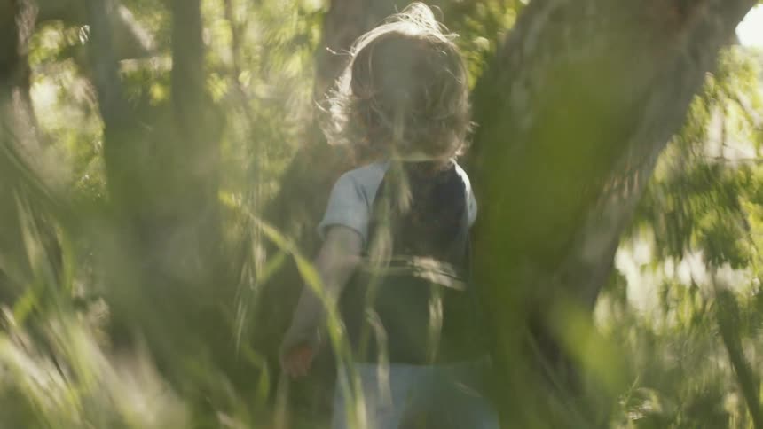 Toddler standing outdoors amongst the grass and trees