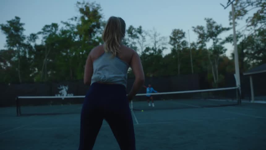 A woman plays tennis with a male opponent on an outdoor court