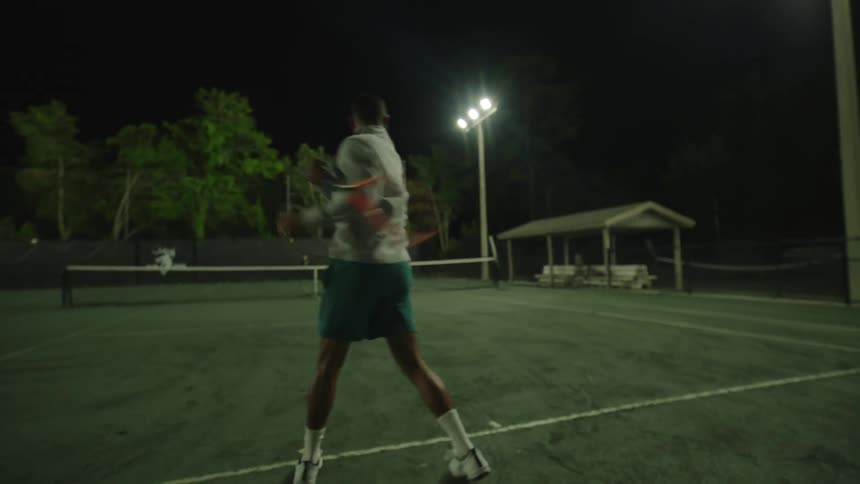 Man playing tennis on a court at night