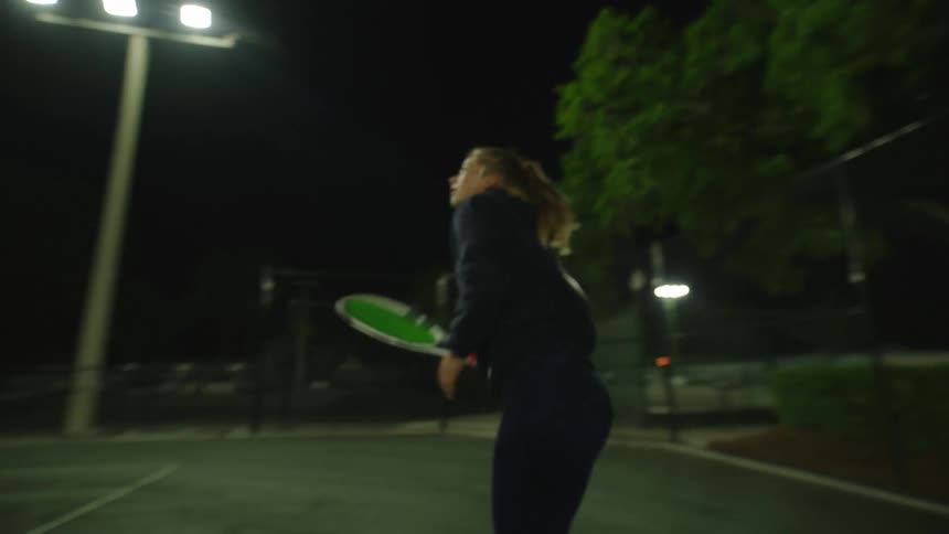 Woman playing tennis on a court at night
