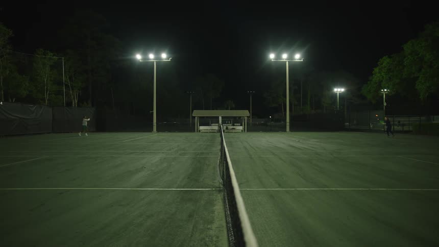 Two people playing tennis on an open air court at night