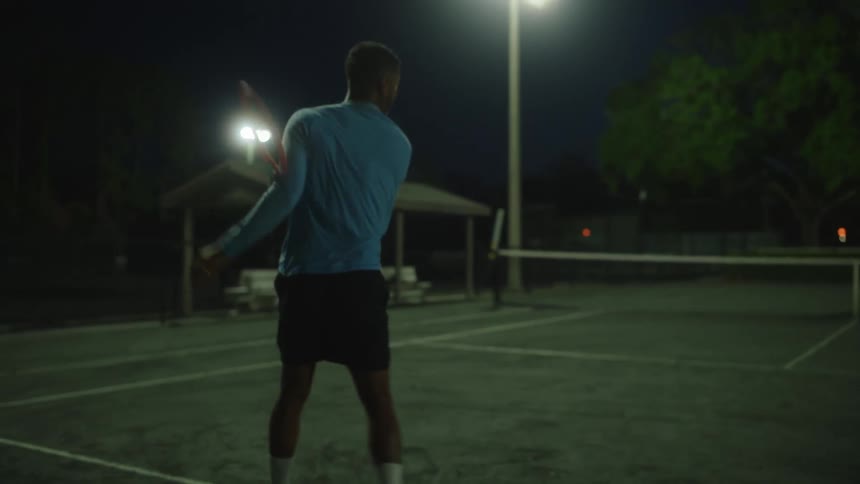 Man playing tennis on a court at night