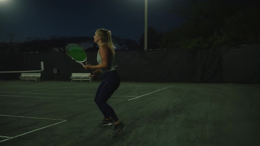 Woman playing tennis on a court at night