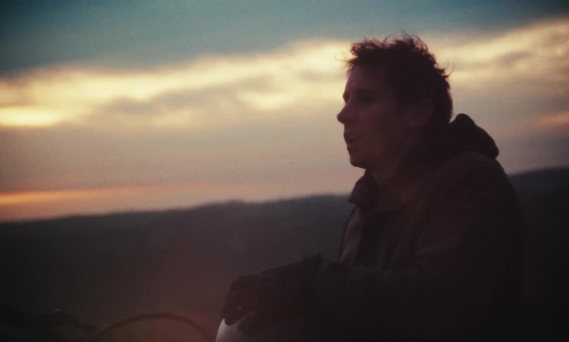 A man sitting on a motorcycle takes out his helmet at dusk