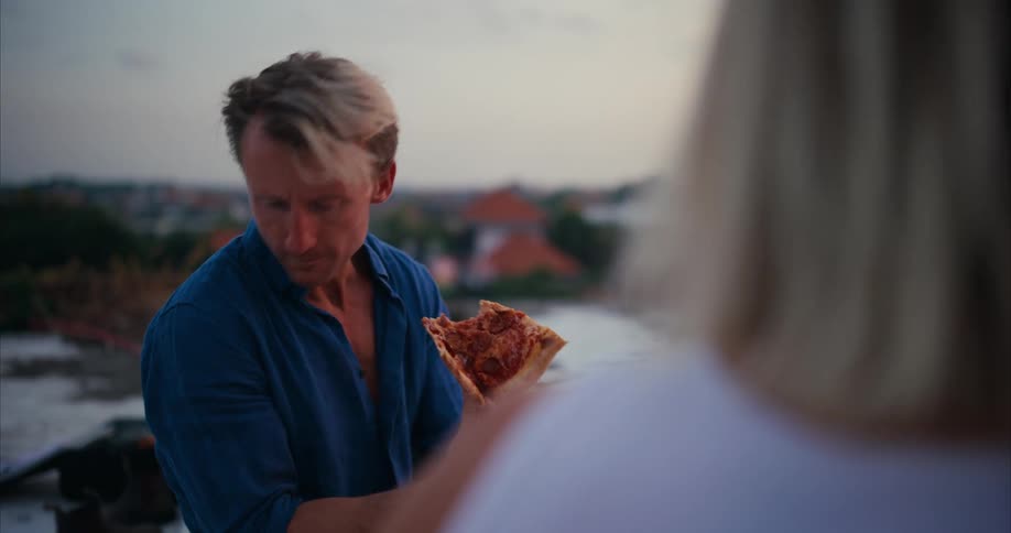 A man teases a woman with a piece of pizza