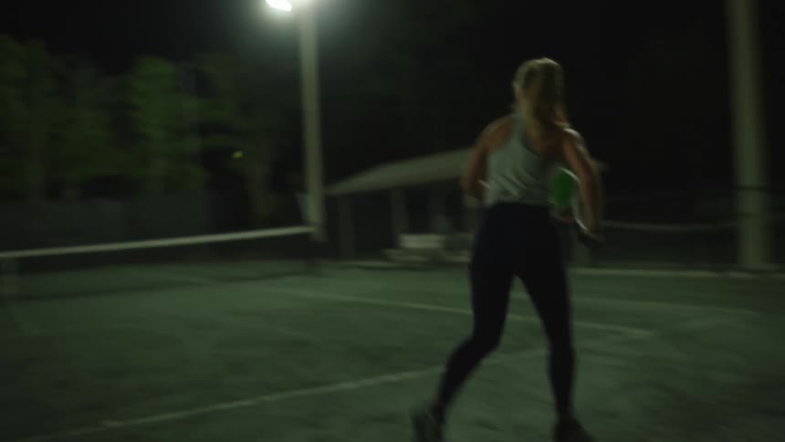 A woman with long hair playing tennis on an outdoor court at night