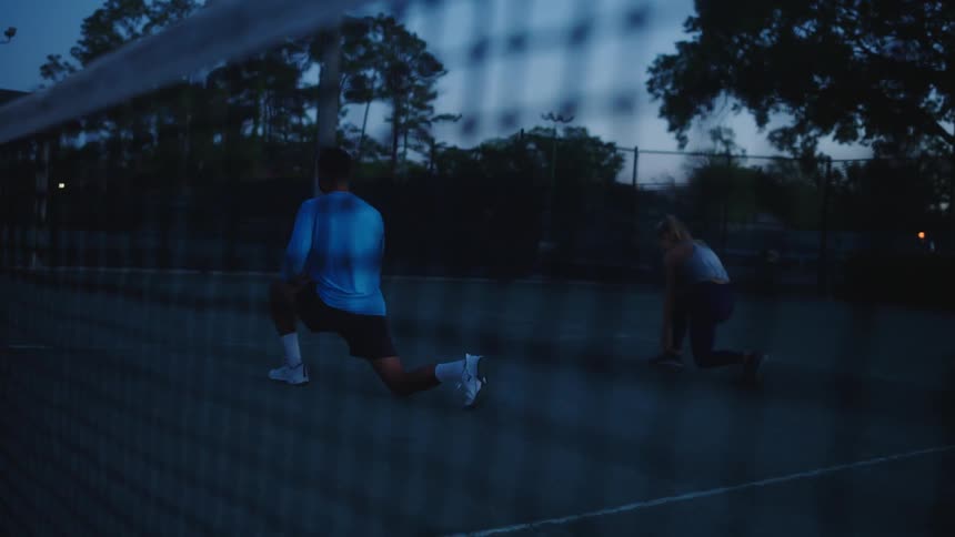 Man and woman in the late afternoon doing squats on a tennis court
