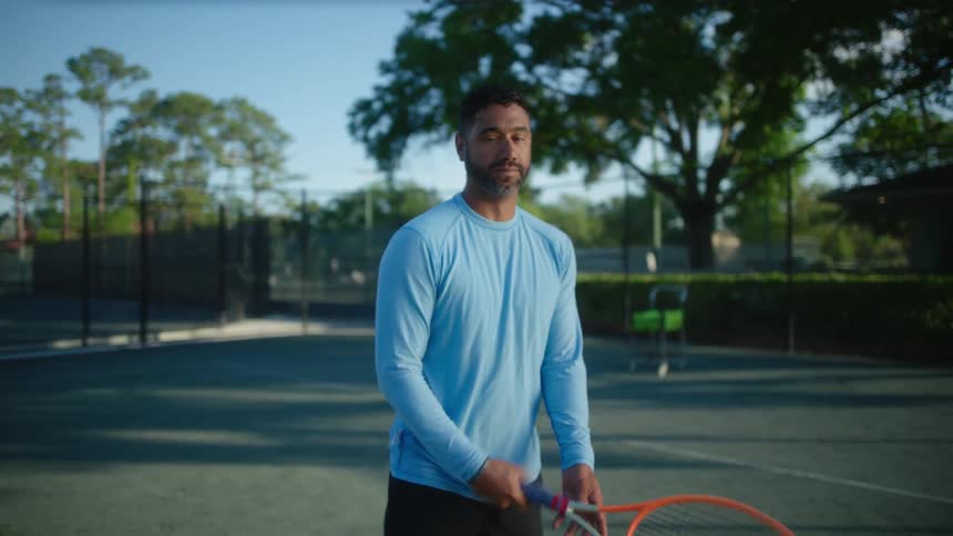 A man stands on a tennis court and flips his racket