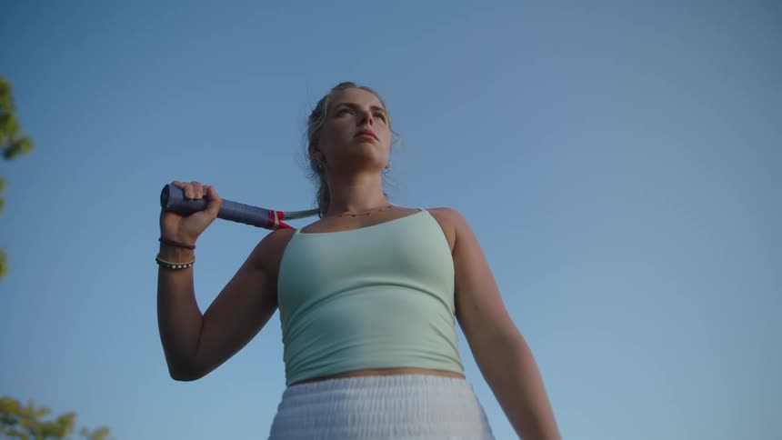 Woman holding a tennis racket behind her back in an openair environment