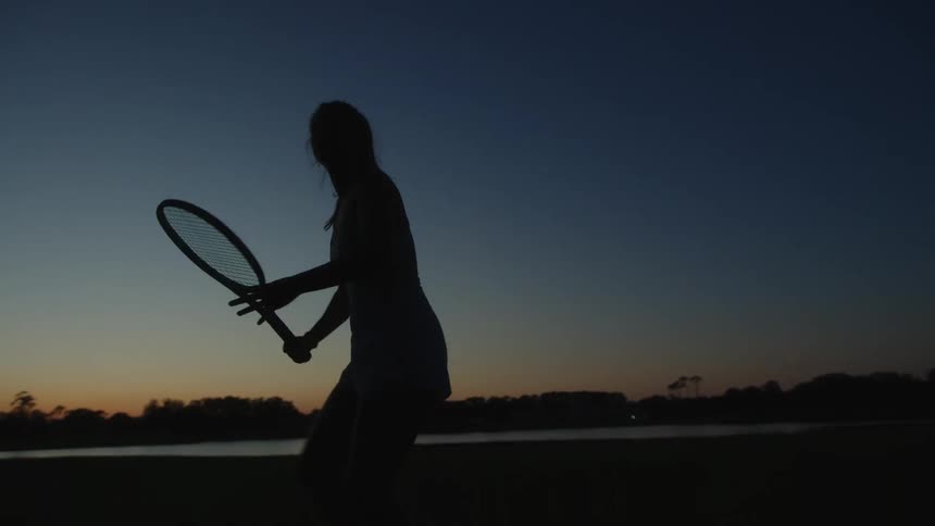 Silhouette of a woman playing tennis against a twilight sky