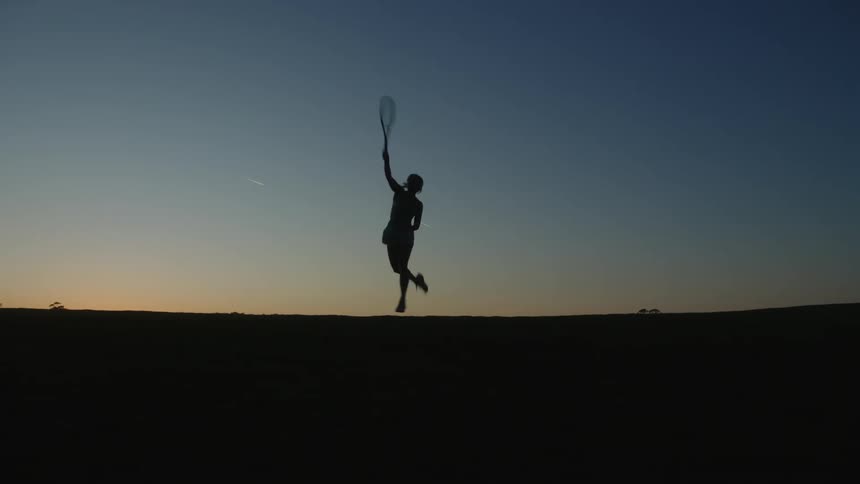 Silhouette of a woman playing tennis against a late afternoon sky