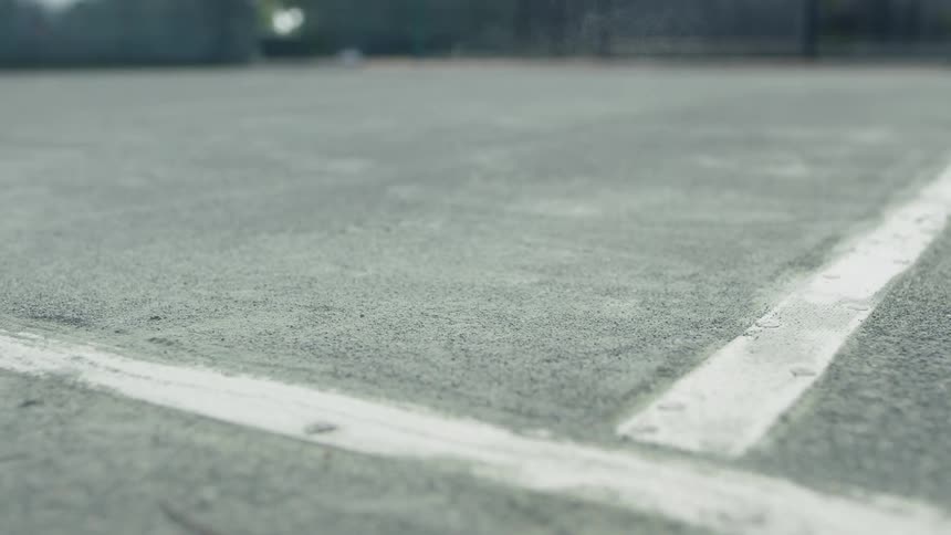 A green tennis ball bounces near the line on the tennis court floor