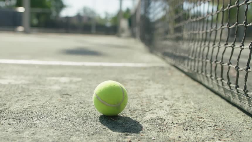 Tennis ball hitting the net and falling on a court during the day