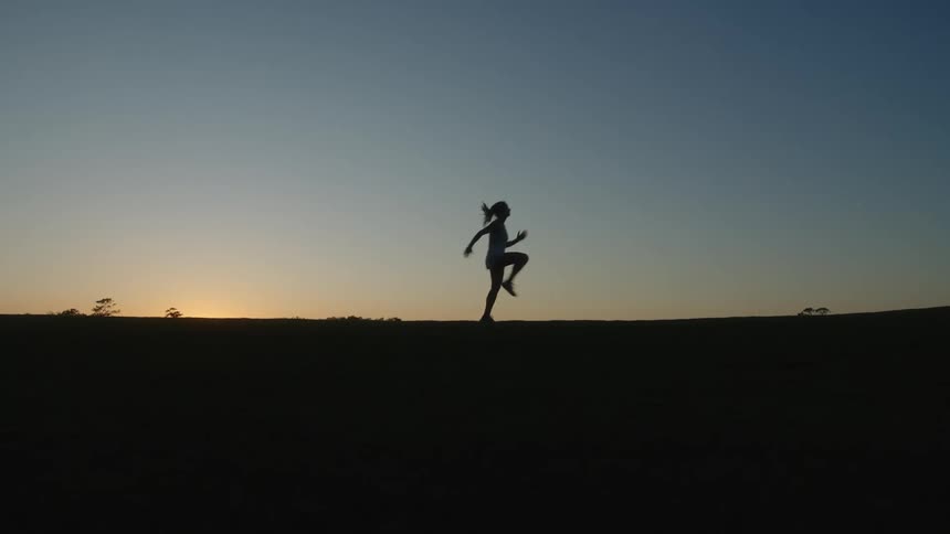 Silhouette of a running woman jumping with her knees up against an evening sky