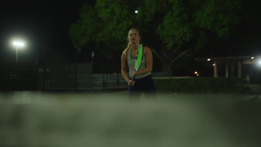 Blonde woman playing tennis on a court at night