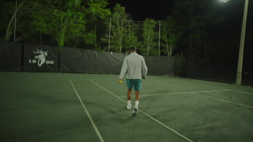 Man holding a racket entering a tennis court at night
