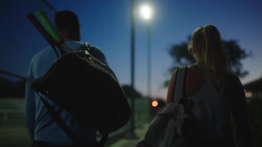Two tennis players walk down a sidewalk next to a tennis court