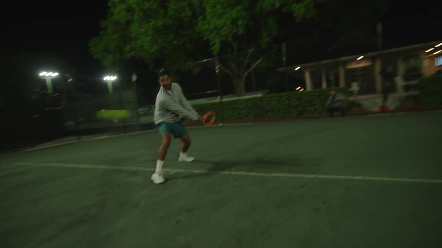 Man playing tennis on a court at night