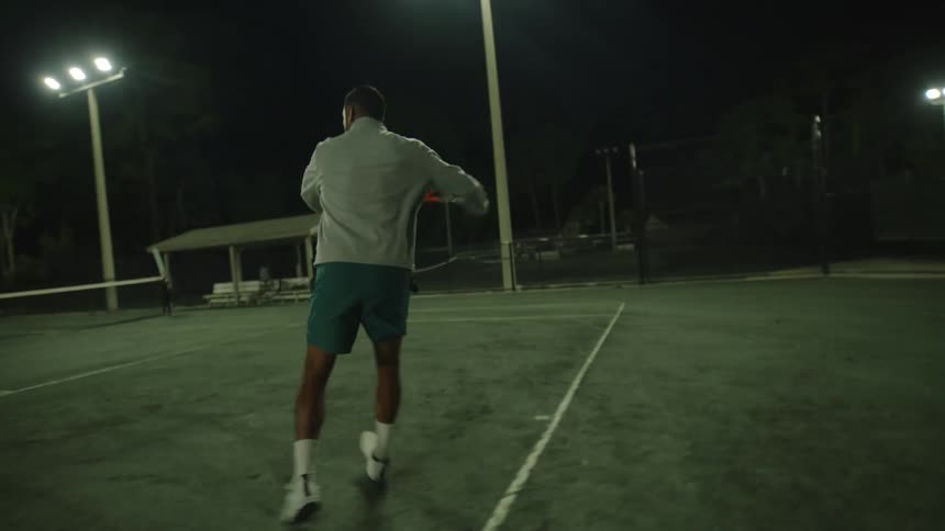 Man playing tennis on a court at night