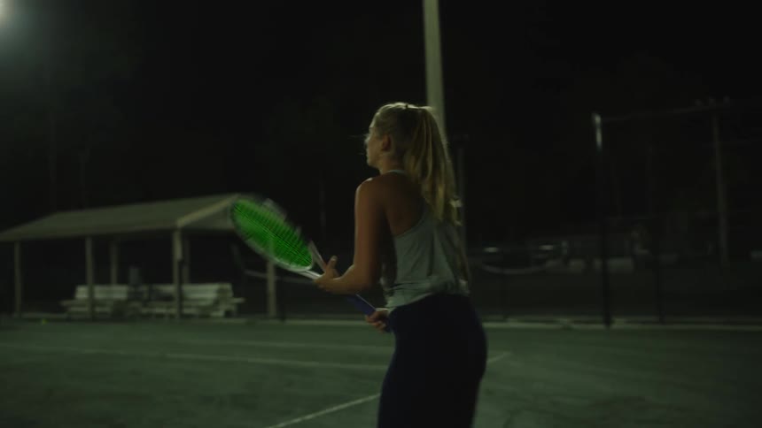 Woman with a tennis racket playing on a court at night