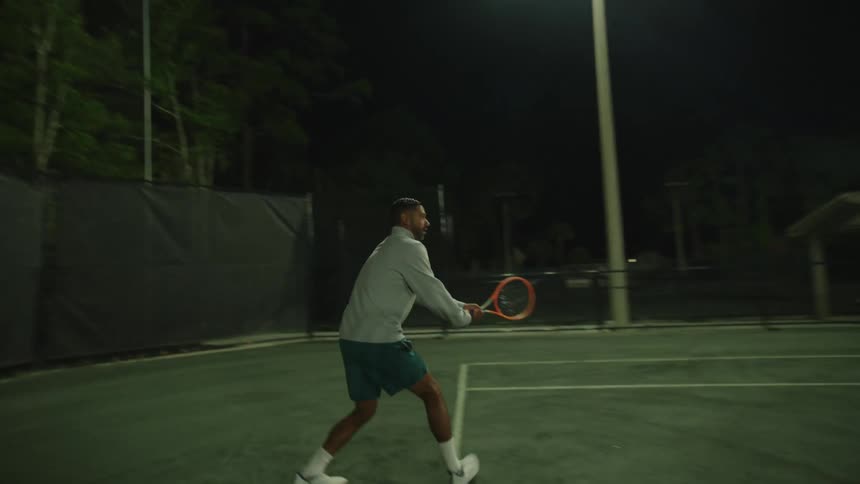 Man with a racket playing tennis on the court at night