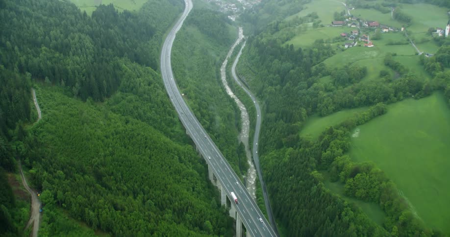Aerial panorama of a winding road amid green mountains and on the edge of a river