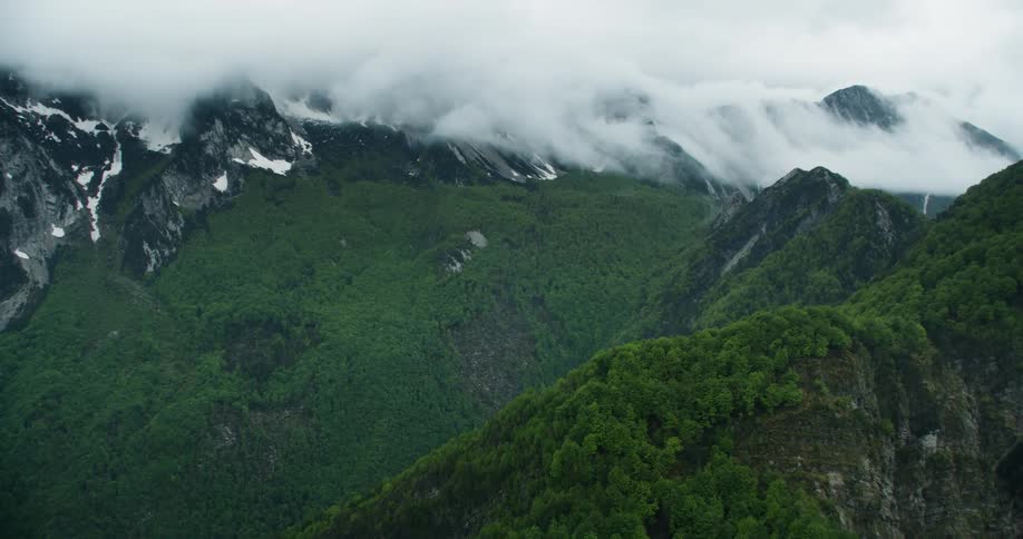 Dense clouds obscure snow dappled mountain top in mountain range