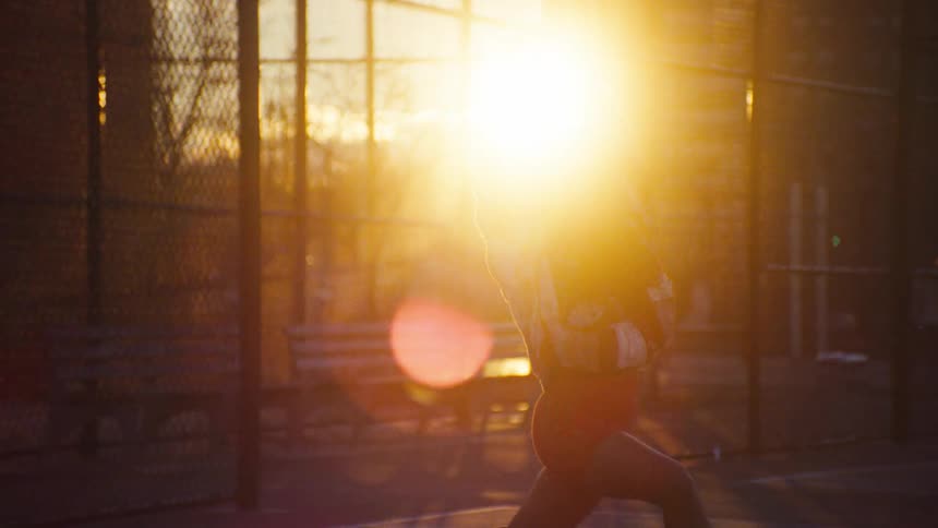 A young woman listening to music and dancing on rollerskates in a street basketball court