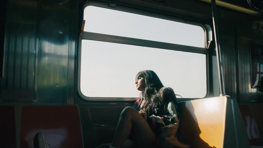 A woman is sitting on a seat of a train and is looking out the window