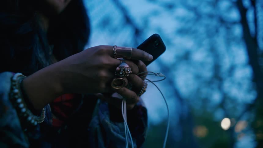 A person with several rings in their hand is using a cell phone and in the other hand holding a white cable