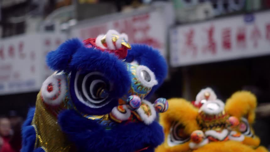 Two people dressed as blue and yellow dragons parading down a street with several people in the stands