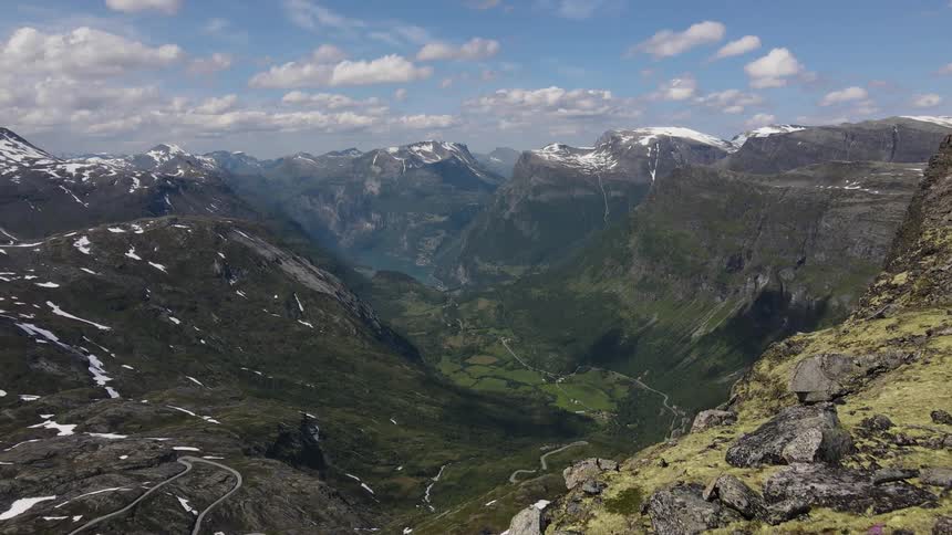 Man on a cliff with a panoramic view of a mountain valley with snowcapped peaks