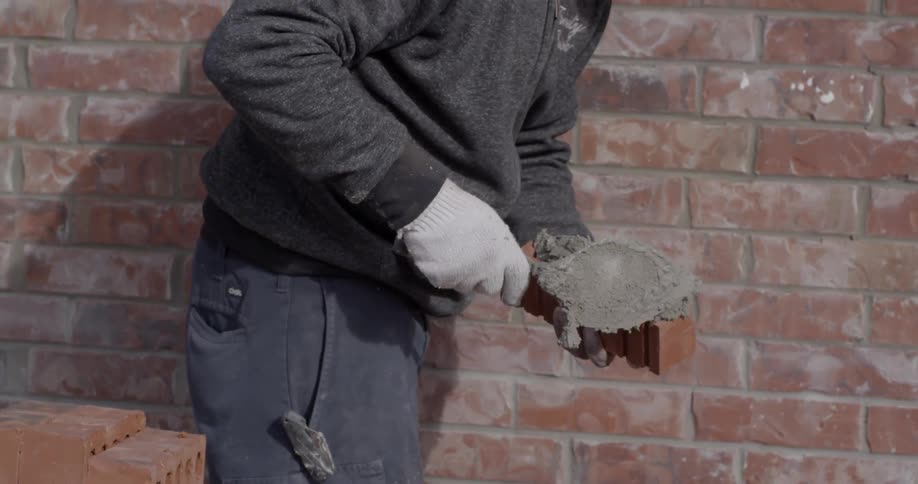A bricklayer scoops up mortar and adds a brick to a wall