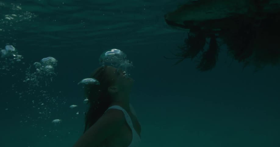 A woman clings to a piece of floating debris in the open ocean surrounded by calm waters and an overcast sky
