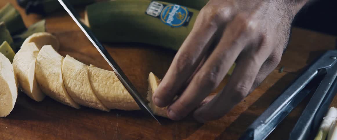 Closeup of a persons hands cutting banana slices with a knife
