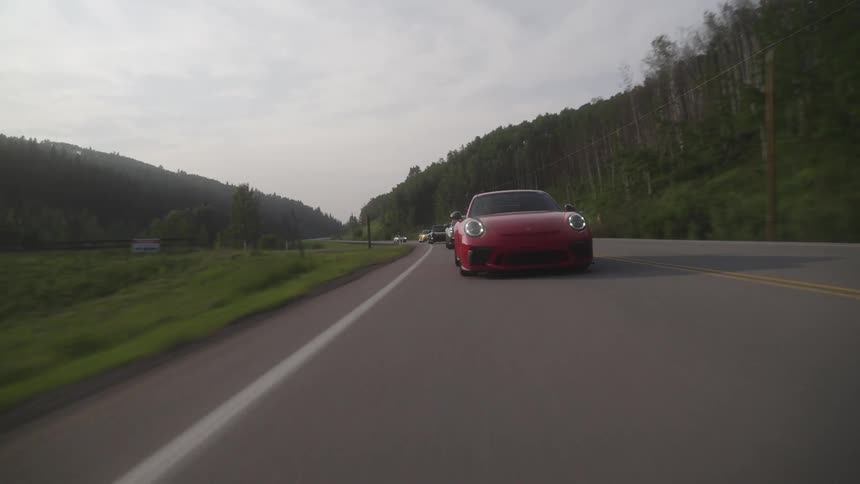 Sports cars driving on a road through a green forested area