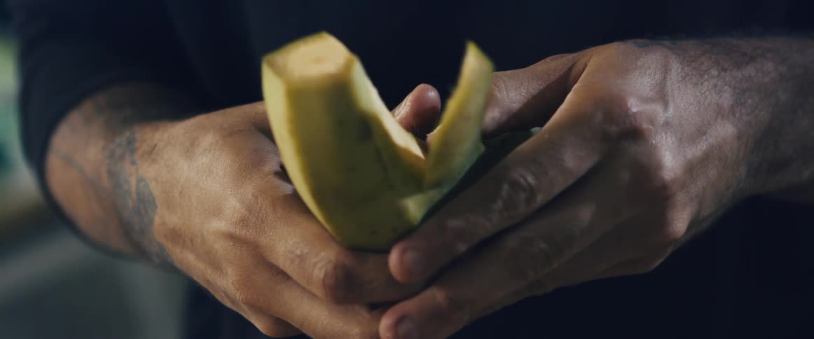A man with tattoos peeling a plantain