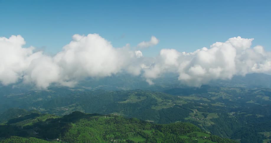 An aerial view of a region with green hills full of trees and white clouds in the sky