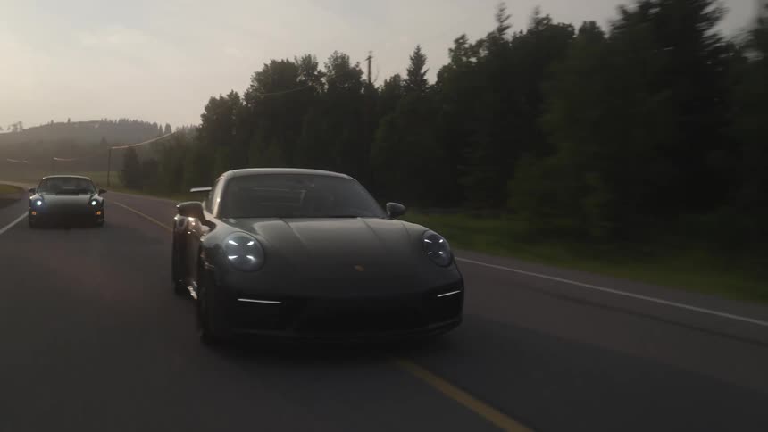 Two porsche driving on a road through the countryside at sunset