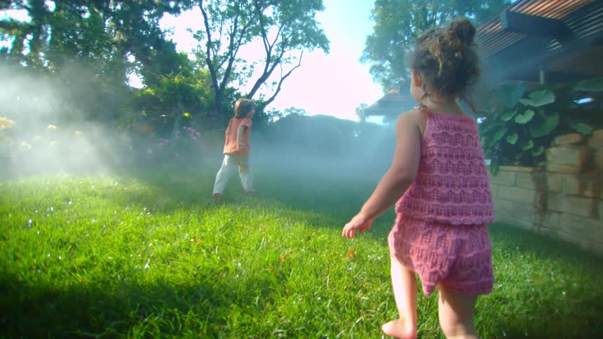 Two children running on the grass in a backyard