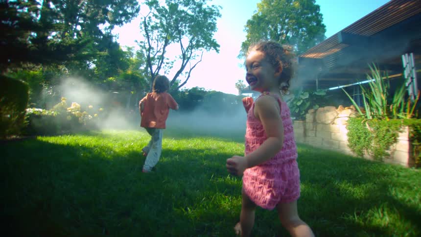Young brother and sister smile while running across lawn near home