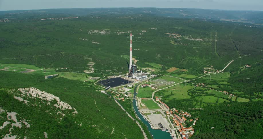 Aerial panorama of a small body of water in the middle of green mountains and a power plant