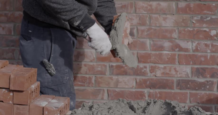 A man is putting concrete on bricks and placing them
