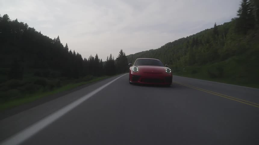 Red porsche and other cars traveling down a road with trees around