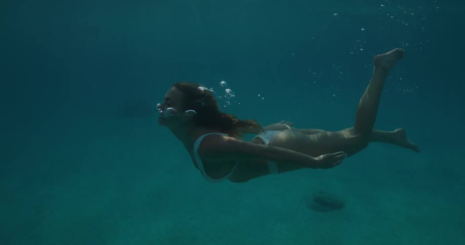 Woman in white bikini swimming submerged in the ocean