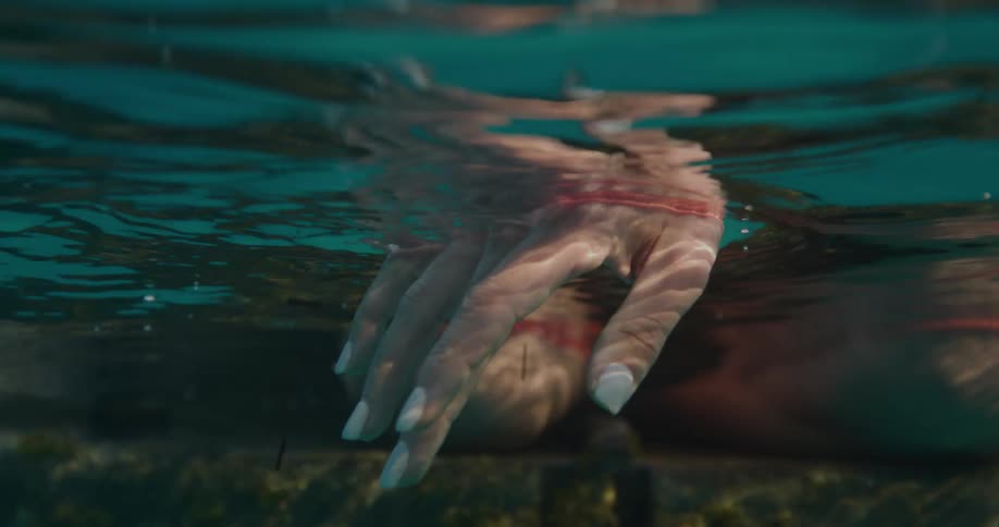 A persons hand partially submerged in water with a reflection visible on the surface