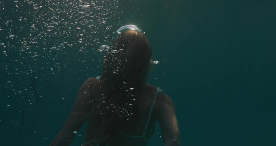 Woman blows bubbles while swimming toward the surface